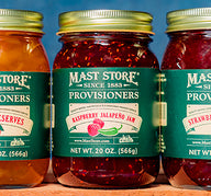 Jars of Mast Store Provisioners Preserves with fruits illustrations on the label, on a blue background.