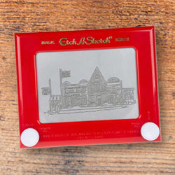 Red Etch-A-Sketch showing a drawn design of the Original Mast Store building on a wooden surface
